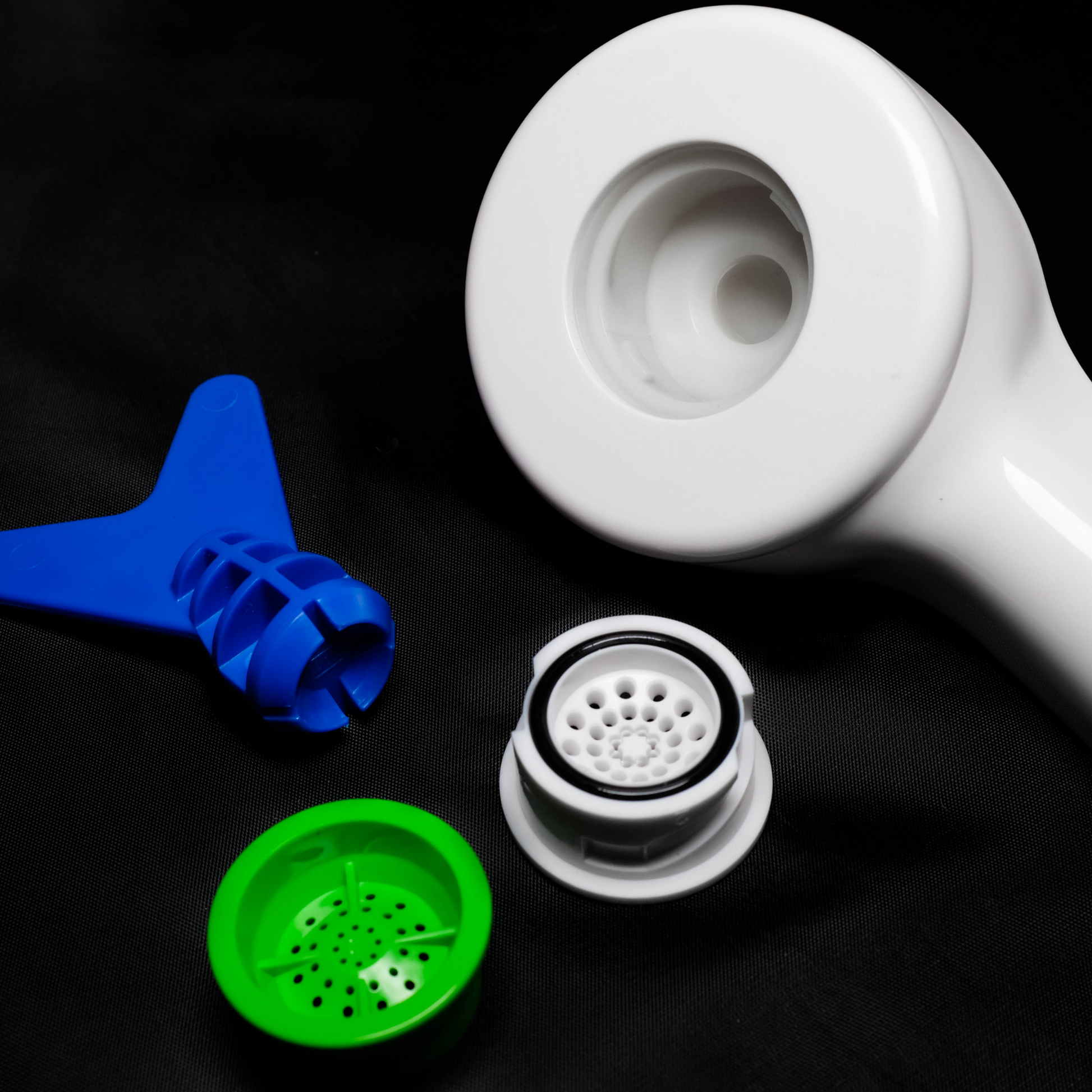 White shower head close up with blue and green accesories on a black background
